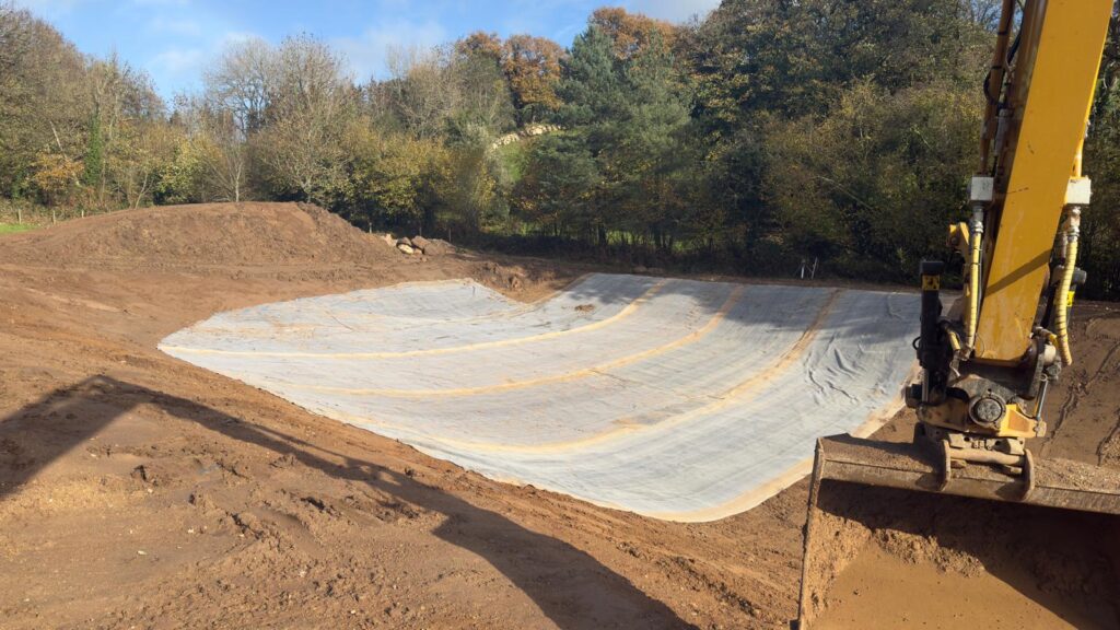 Partially completed wildlife pond showing the hole dug out and the liner being installed
